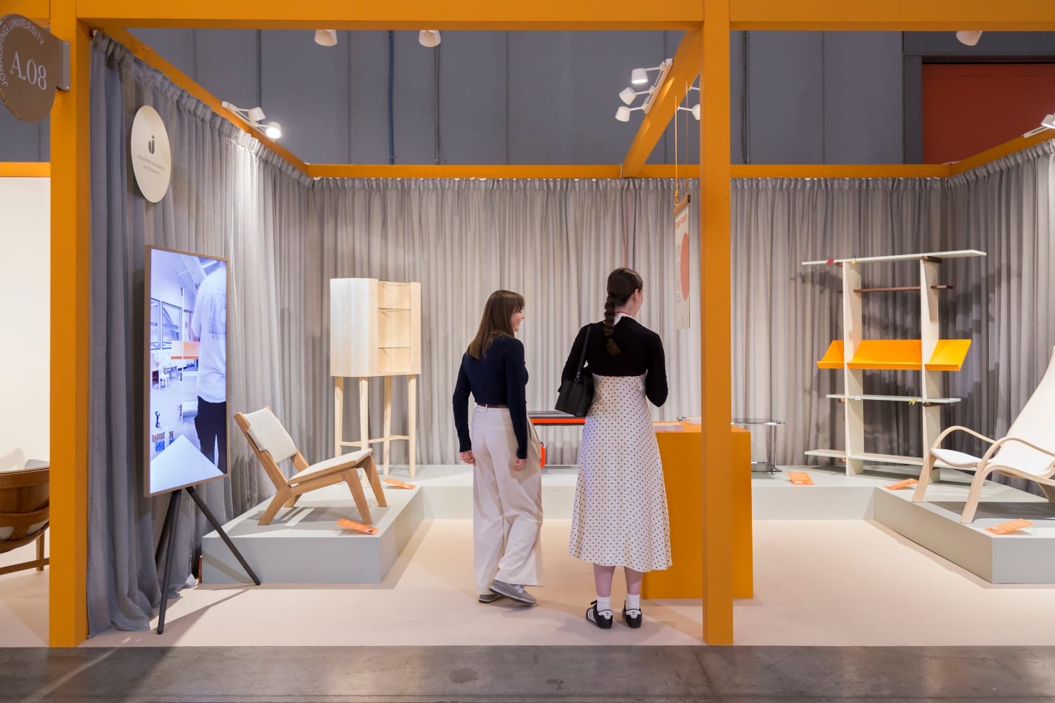 Visitantes exploram estande de design no Salone del Mobile Milano, com móveis contemporâneos expostos em ambiente com estrutura colorida e curadoria de produtos