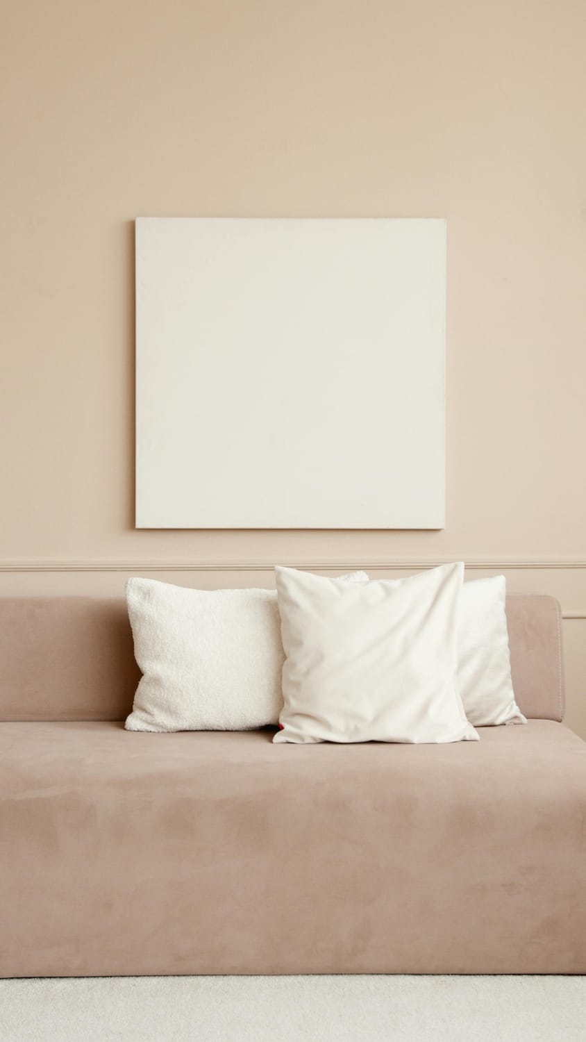 Sofá em tons neutros com almofadas claras e quadro minimalista em parede bege