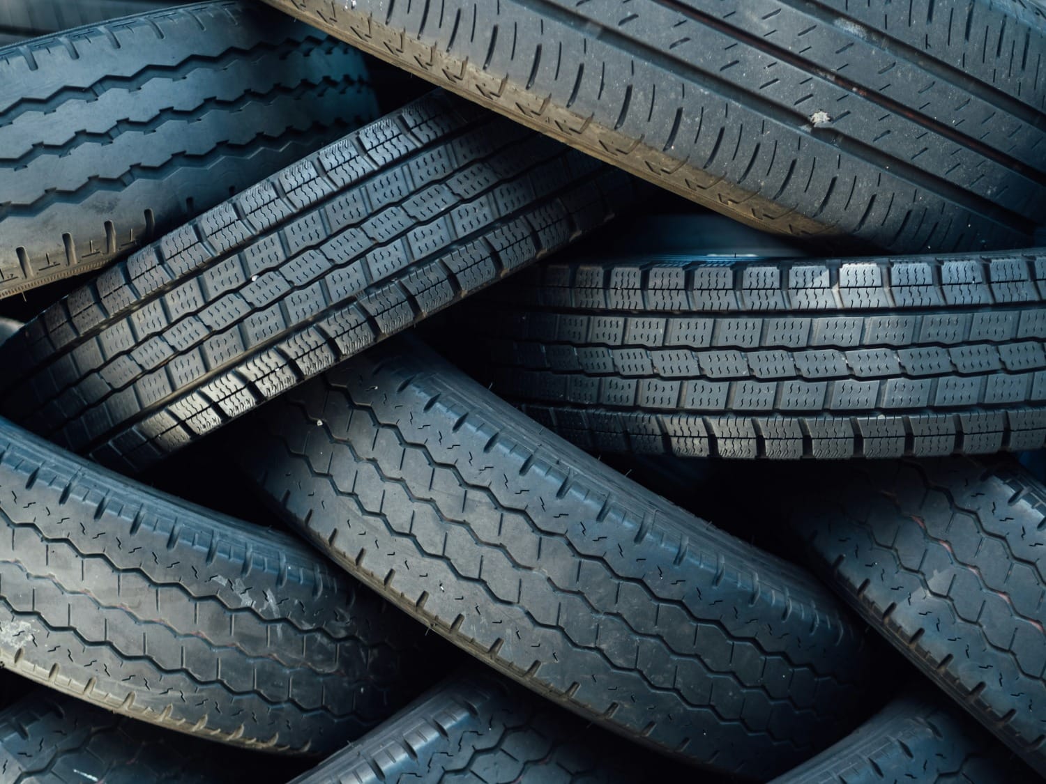 Pilha de pneus usados com diferentes padrões de desgaste, destacando reciclagem de borracha, reaproveitamento e impacto ambiental de resíduos automotivos