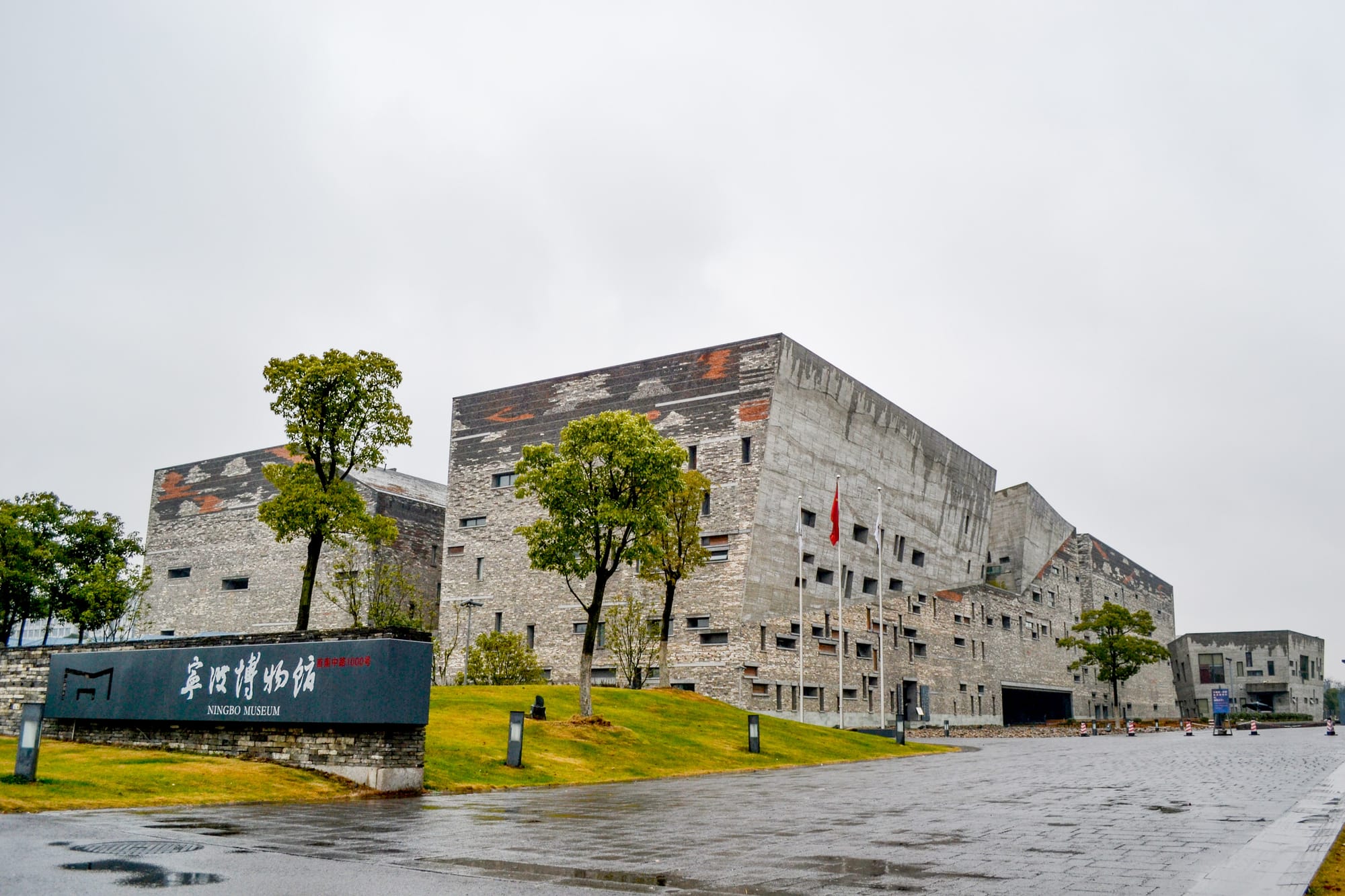 Vista externa do Museu de Ningbo, na China, com arquitetura contemporânea marcada pela combinação de concreto aparente, tijolos reciclados e volumes geométricos integrados à paisagem urbana