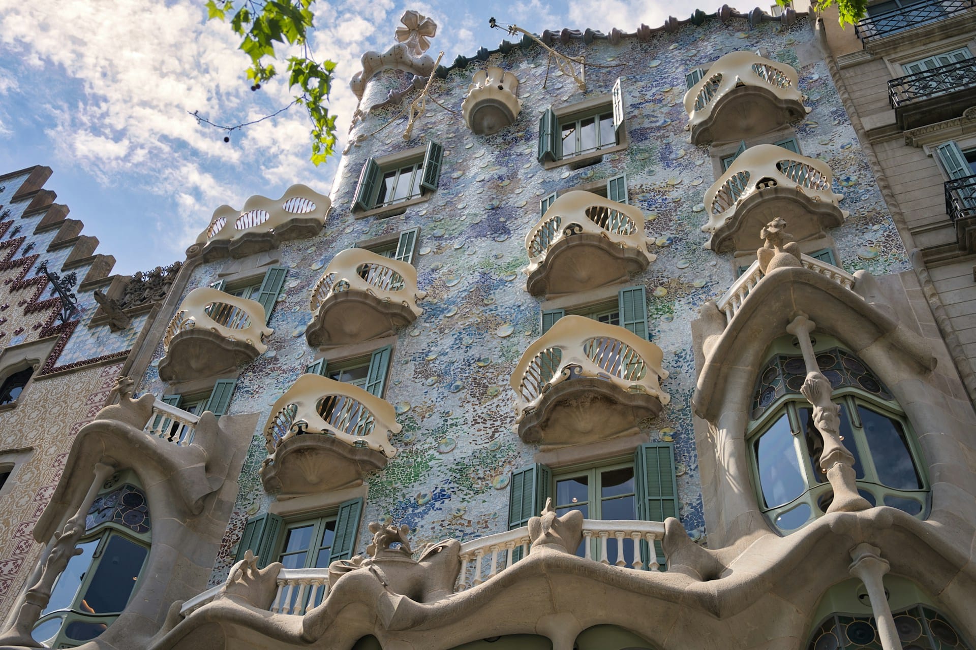 A fachada da Casa Batlló, em Barcelona, é revestida por um mosaico de fragmentos cerâmicos e vidro que refletem a luz de maneiras diferentes ao longo do dia. As varandas de formas orgânicas parecem esculturas moldadas pela natureza, enquanto as linhas curvas da fachada eliminam qualquer rigidez geométrica.
