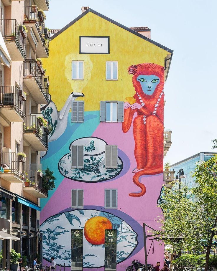 Gucci ArtWall – Largo La Foppa, Milão (2018) Criado pela ilustradora britânica Alex Merry, este mural integrou a campanha Gucci Décor e transformou uma fachada urbana em uma galeria de arte a céu aberto. A obra reúne elementos da coleção de decoração da Gucci em uma composição vibrante, reafirmando o diálogo entre moda, ilustração e arquitetura.