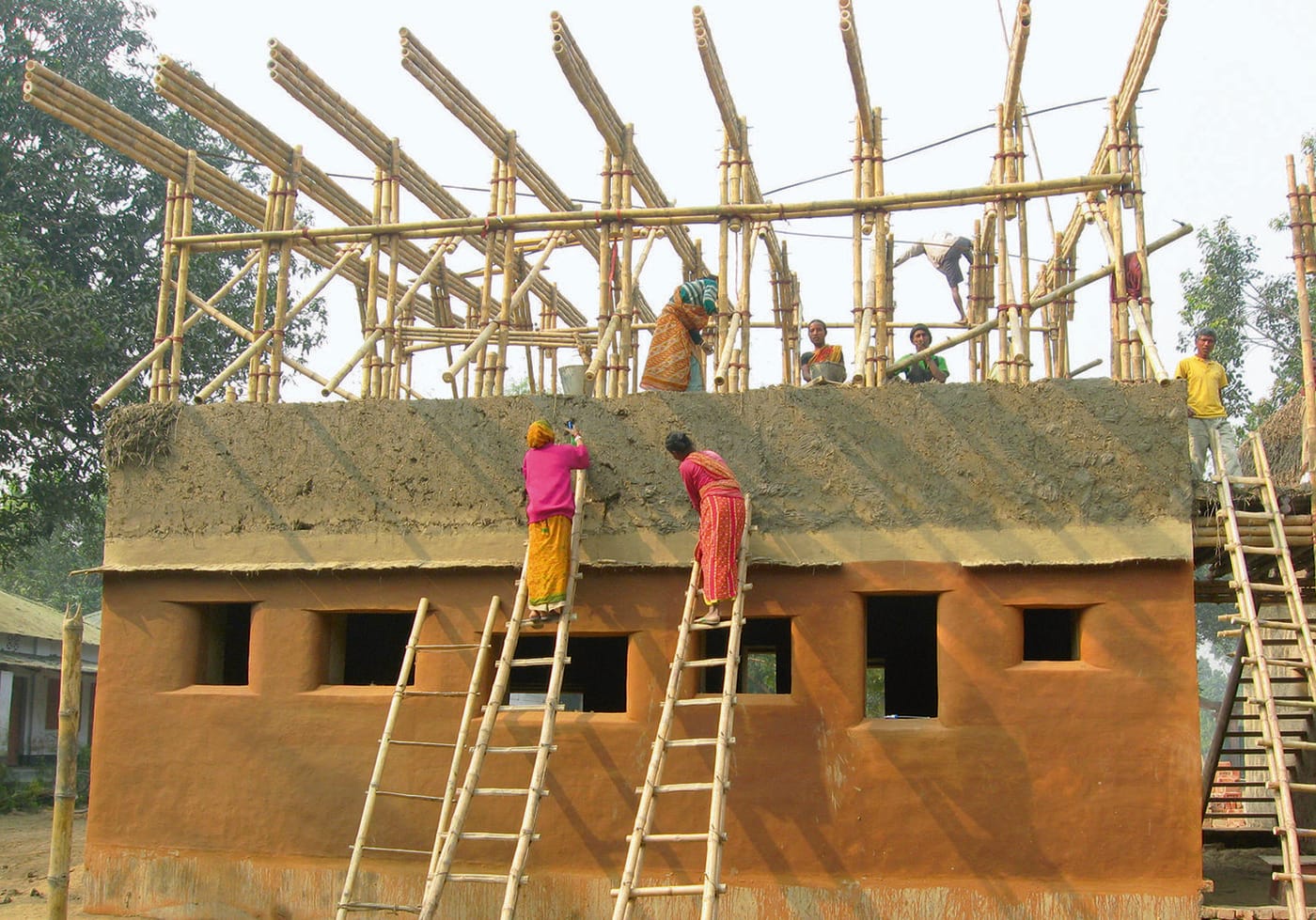 Trabalhadores aplicando terra na parede do centro Desi, sobre escadas de bambu