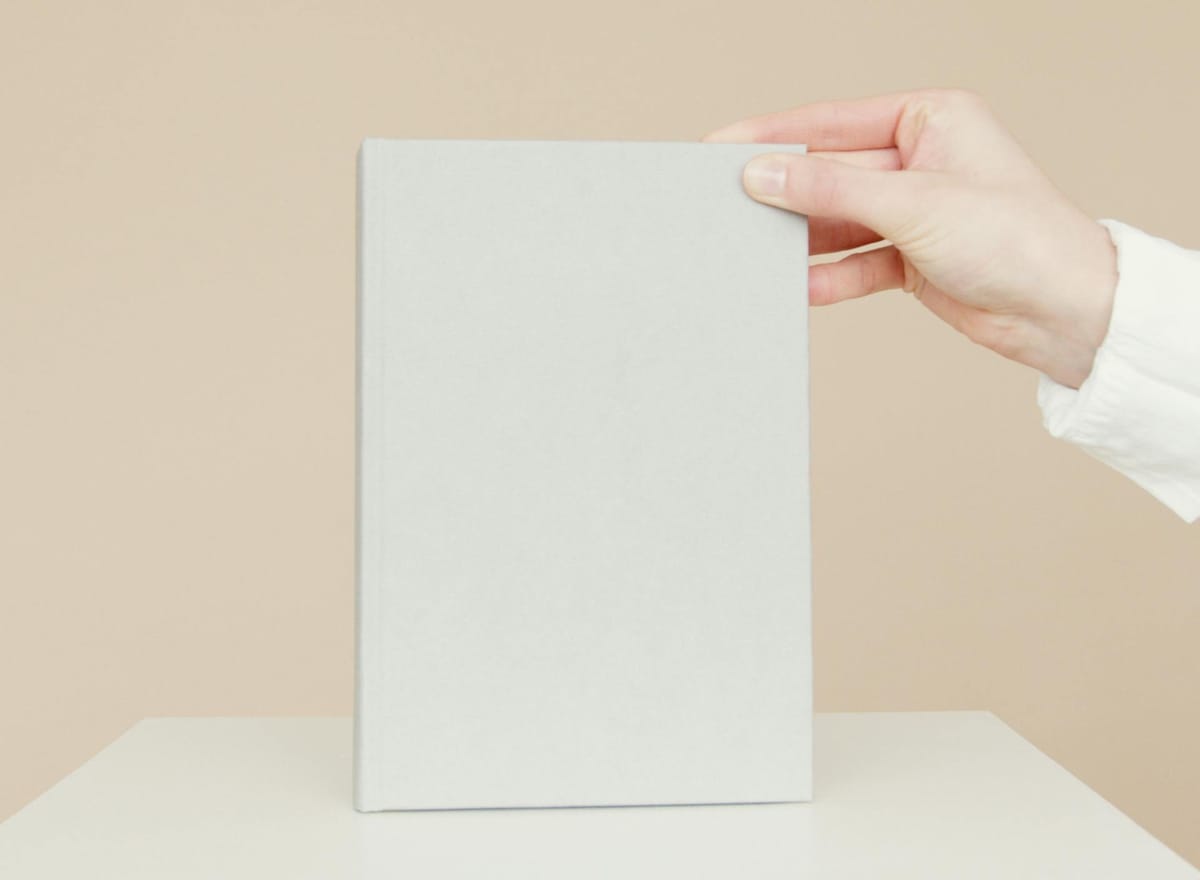 Mão segurando revestimento cinza minimalista sobre mesa clara, em fundo neutro bege