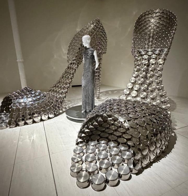 Instalação da artista Joana Vasconcelos na exposição "VENUS": esculturas metálicas em forma de sapatos gigantes cercam manequim com vestido prateado