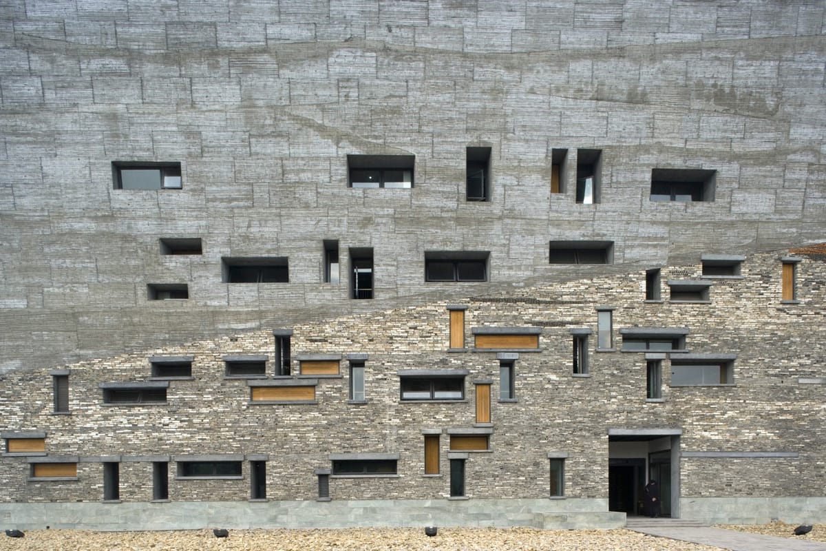 Fachada do Museu de Ningbo, edifício com revestimento em concreto aparente e pedra natural, destacando janelas irregulares