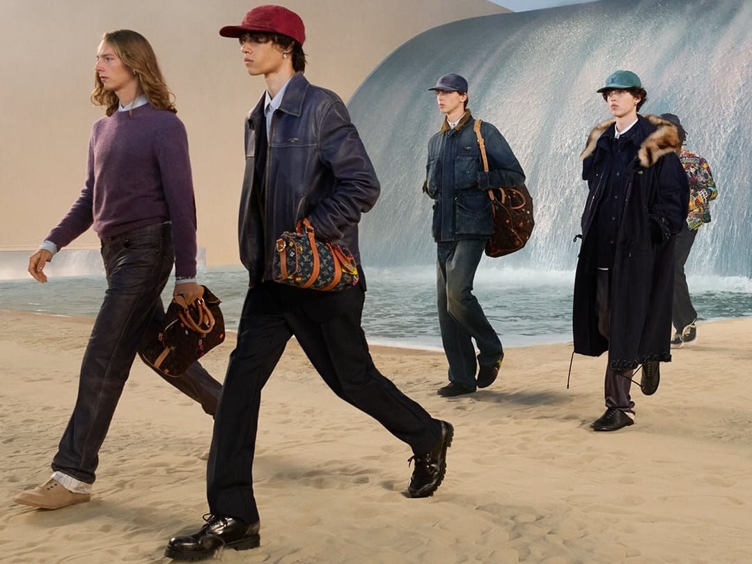 Desfile masculino da Louis Vuitton apresenta modelos caminhando sobre uma passarela de areia diante de uma instalação em forma de onda, usando peças da coleção assinada por Pharrell Williams