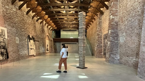 Interior da Punta della Dogana, em Veneza: galeria de arte contemporânea com paredes de tijolo aparente, estrutura de madeira no teto e instalação vertical de livros ao centro