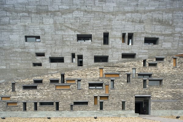 Fachada do Museu de Ningbo, edifício com revestimento em concreto aparente e pedra natural, destacando janelas irregulares